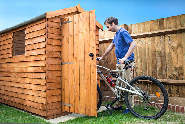 a man keeping his bike into a wooden storage shed